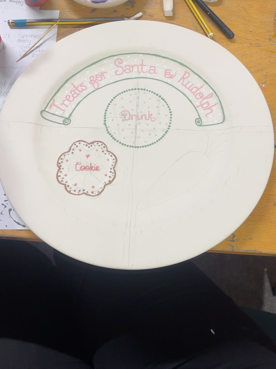 Hand-painted Christmas Eve plate in progress with red lettering, green dotted drink circle and iced cookie