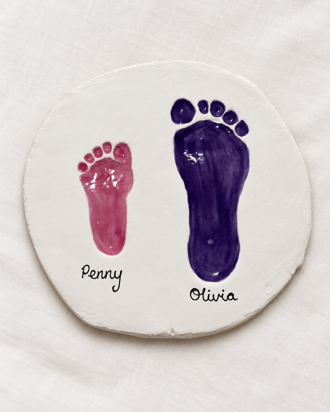Handmade white ceramic keepsake plaque showing Penny and Olivia's pink and purple glazed footprints in clay