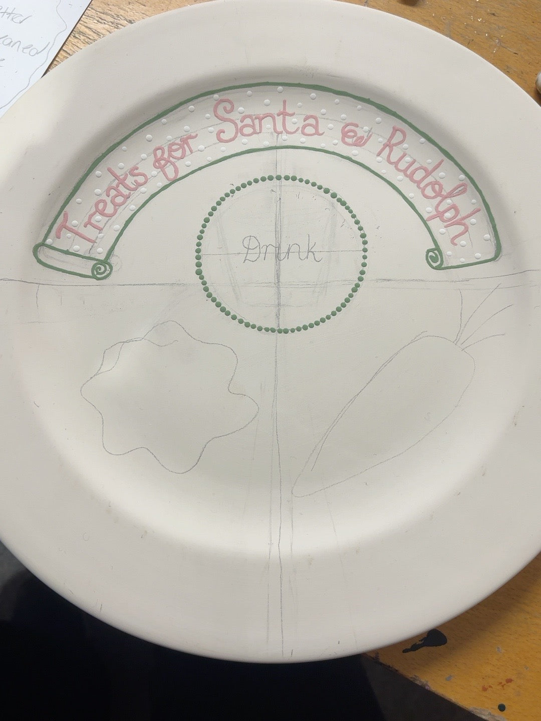 Hand-lettered Santa and Rudolph banner with green scroll border on unfinished Christmas Eve ceramic plate