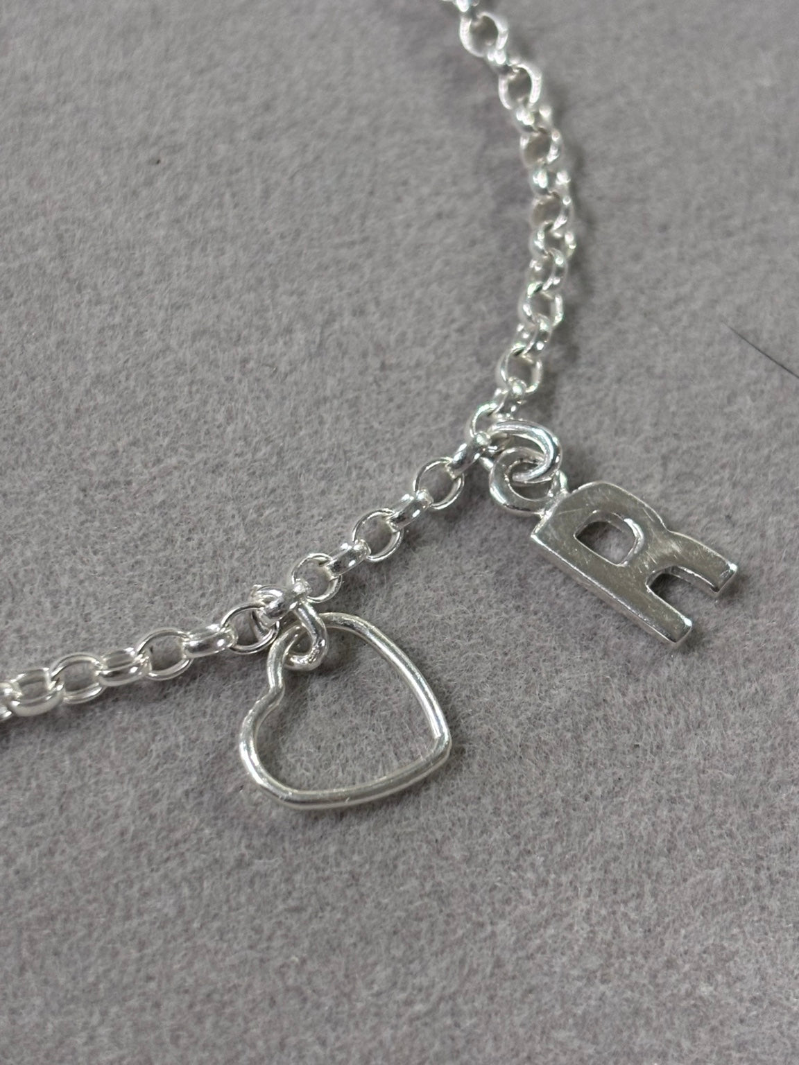 Detailed view of polished 925 sterling silver R initial and open heart charm